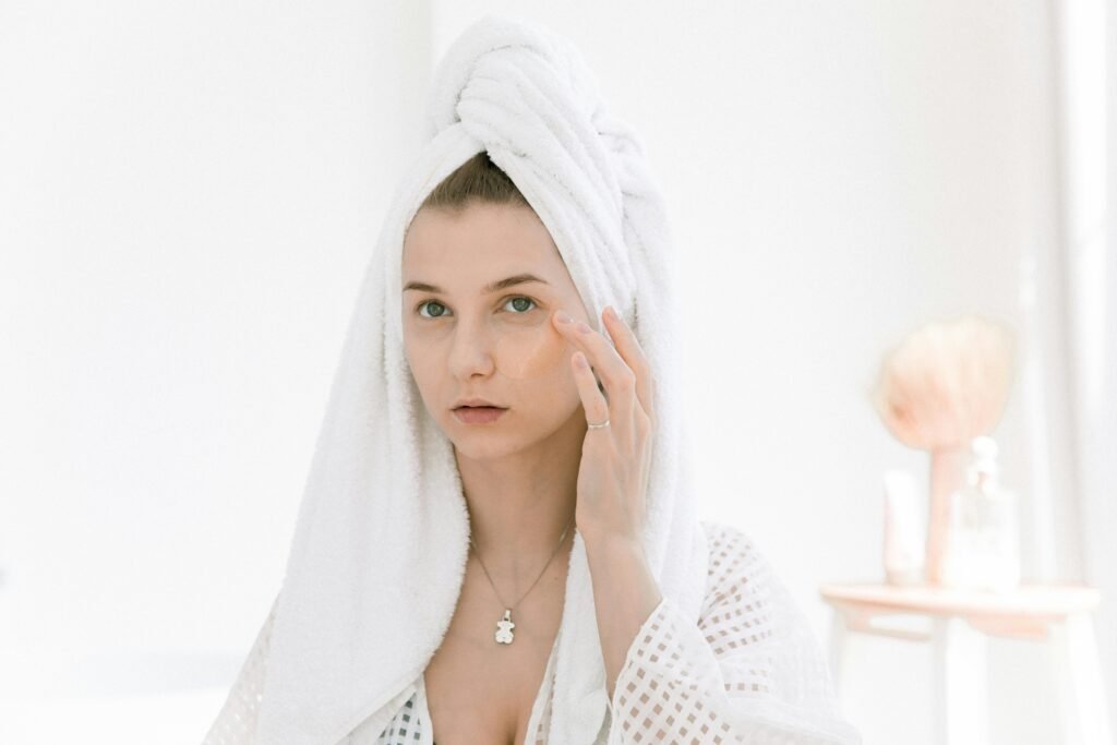A woman in a bathrobe applying skincare products in a bright indoor setting.